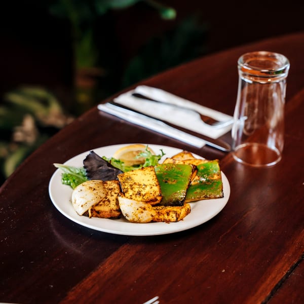 Grilled paneer, onions, and green peppers with a lemon wedge on a white plate at Cinnamon Indian Restaurant.