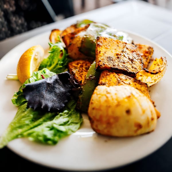Indian paneer tikka with green peppers, lettuce, and a lemon wedge on a white plate.