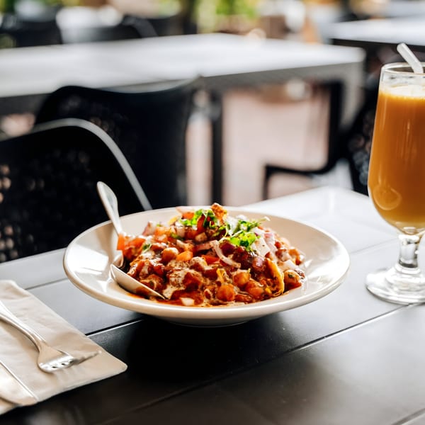 A plate of Indian chana chaat with a glass of mango lassi on an outdoor table.
