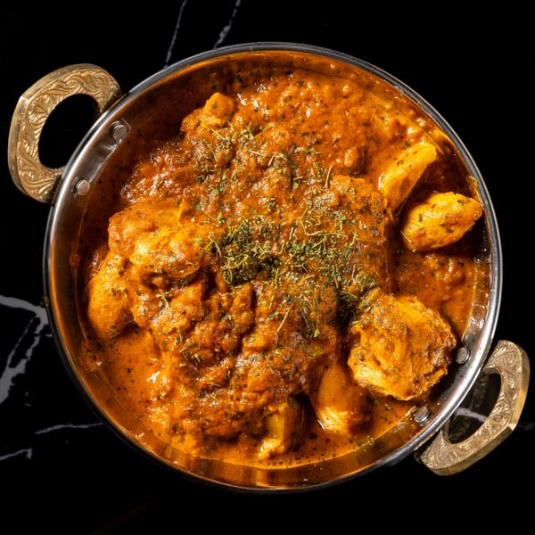 Overhead view of chicken tikka masala in a traditional metal karahi bowl with ornate handles.