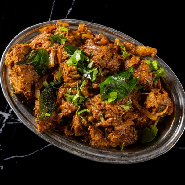 Spicy Indian goat curry, garnished with fresh cilantro and curry leaves, served in a silver dish.