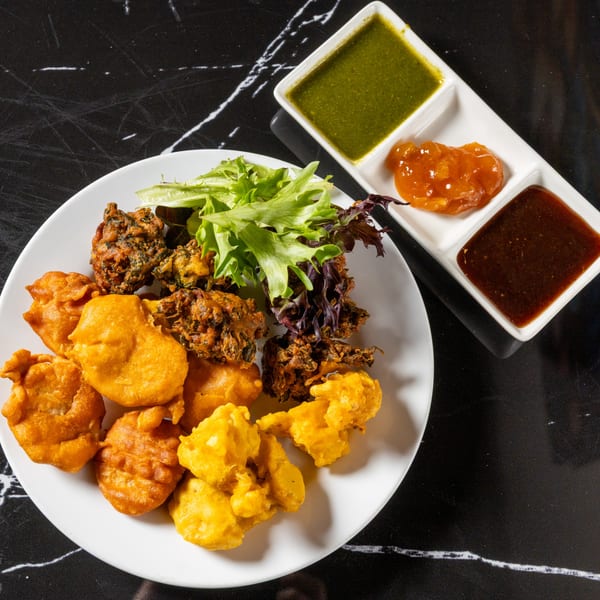 A plate of golden-fried pakoras and vegetable fritters with a side salad and three dipping sauces.