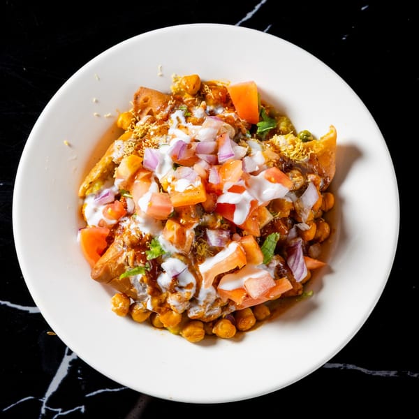 Chana Chaat in a white bowl, topped with yogurt, diced tomatoes, and red onions.
