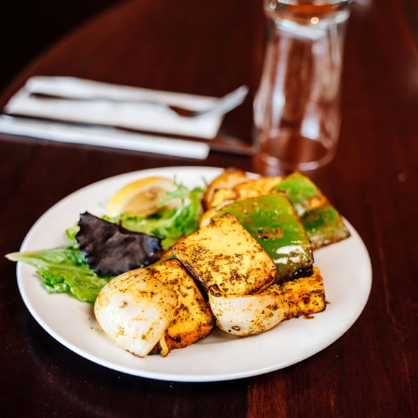 Indian paneer tikka with green peppers, onions, and a side salad on a white plate.