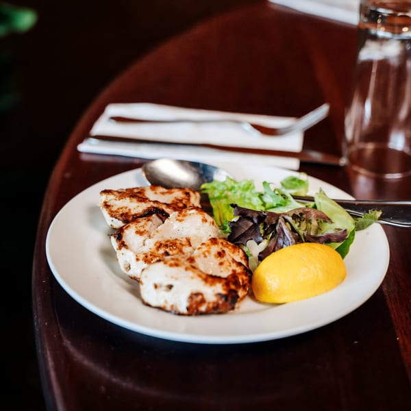 Grilled chicken pieces with a side salad and lemon wedge on a white plate at Cinnamon Indian Restaurant.